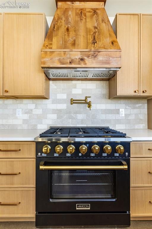 Kitchen featuring premium range hood, light brown cabinets, high end black range oven, and backsplash