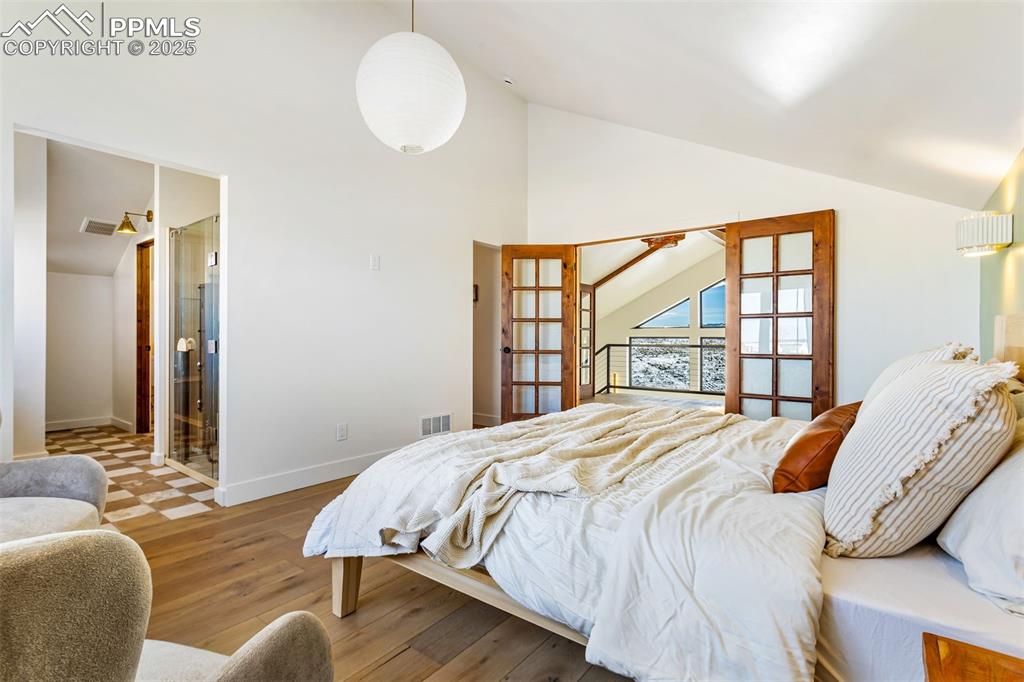 Bedroom featuring wood finished floors, french doors, high vaulted ceiling, and connected bathroom