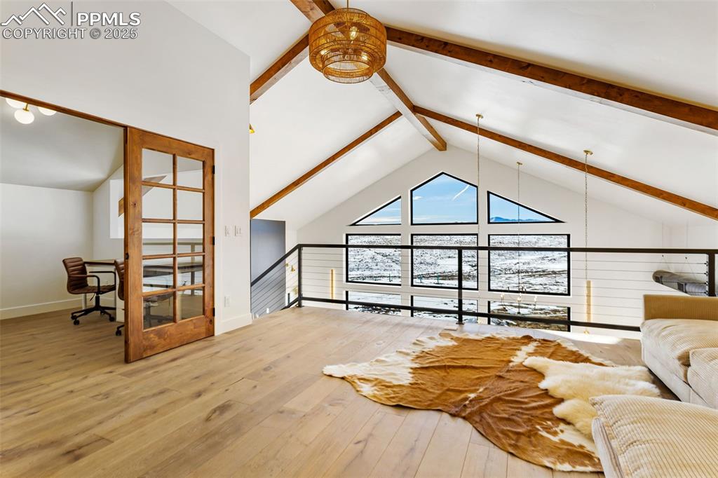 Living room with beamed ceiling, light wood-style floors, a desk, and high vaulted ceiling