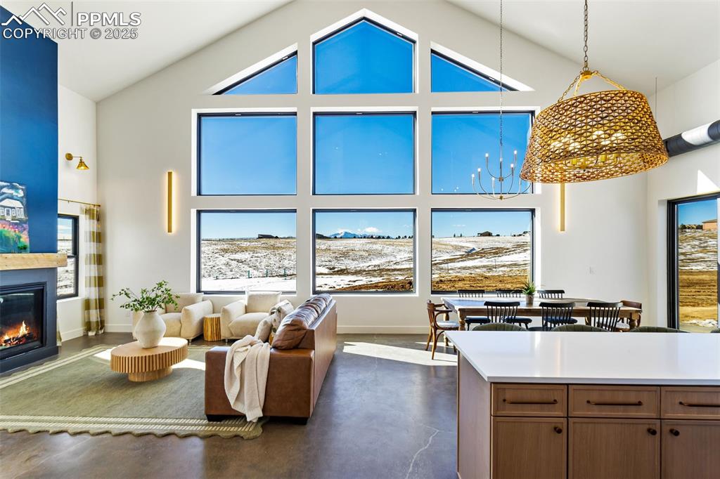 Living area featuring high vaulted ceiling, a glass covered fireplace, a chandelier, and concrete floors