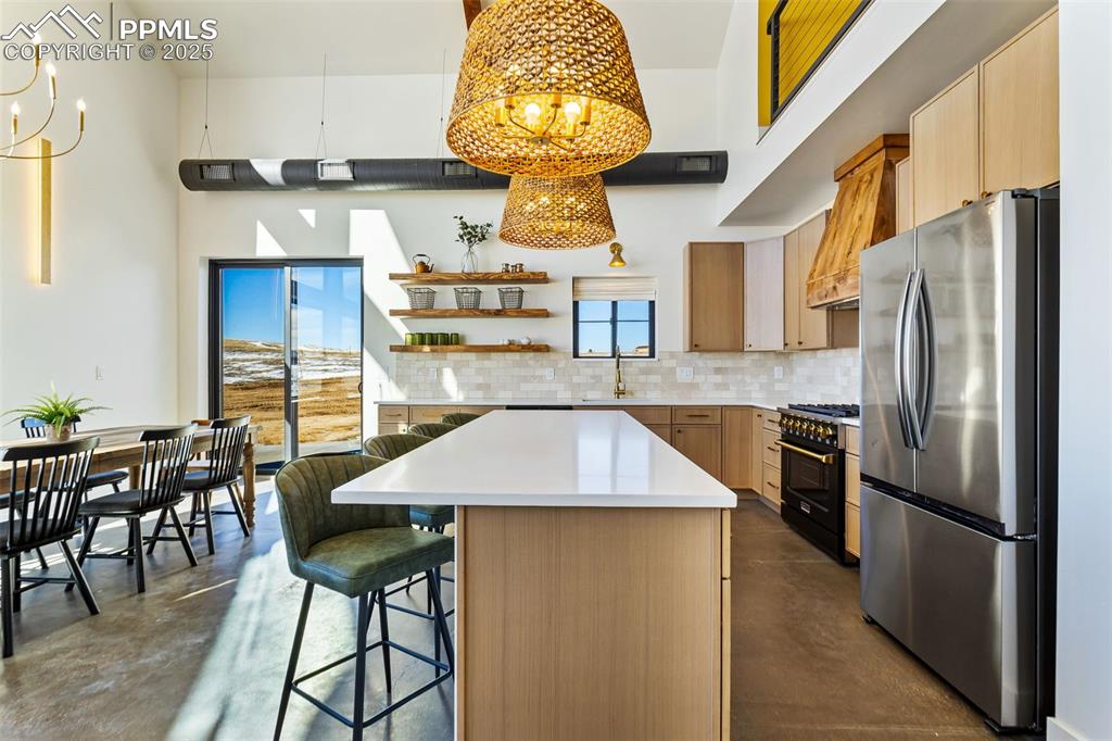 Kitchen with freestanding refrigerator, finished concrete flooring, a chandelier, backsplash, and a high ceiling