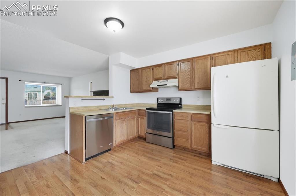 Kitchen with appliances with stainless steel finishes, light countertops, light wood-style floors, under cabinet range hood, and brown cabinets