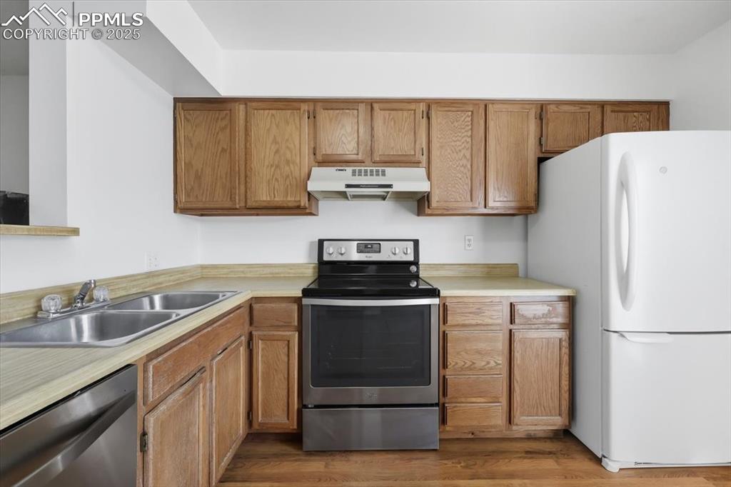 Kitchen with stainless steel appliances, under cabinet range hood, light countertops, and light wood-type flooring