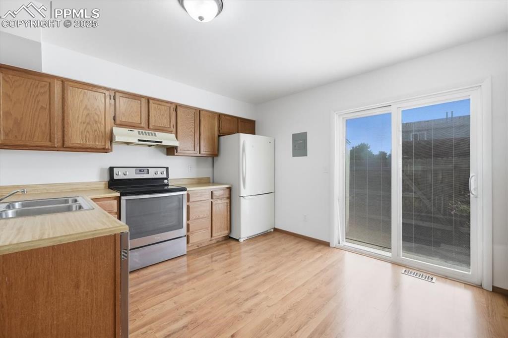 Kitchen with stainless steel electric range, light countertops, freestanding refrigerator, light wood-style floors, and under cabinet range hood