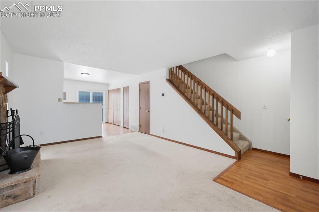 Unfurnished living room with a fireplace, stairway, carpet, and wood finished floors