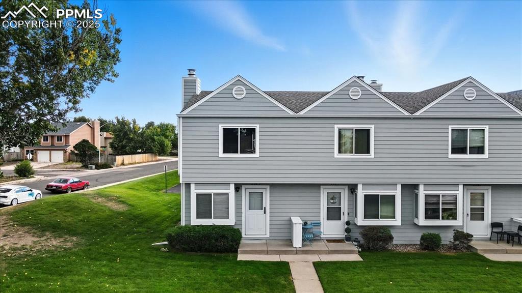 Rear view of property featuring a lawn, a chimney, and roof with shingles