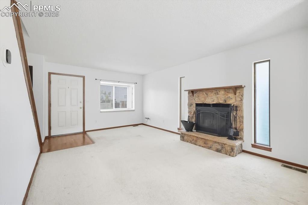 Unfurnished living room with a stone fireplace and carpet