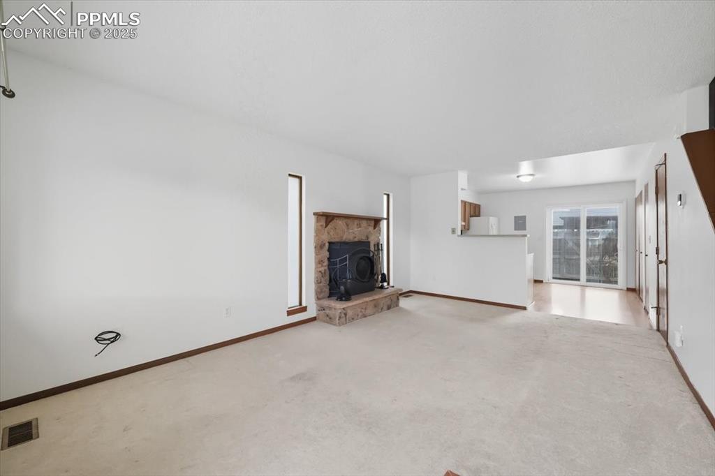 Unfurnished living room with a wood stove and light colored carpet