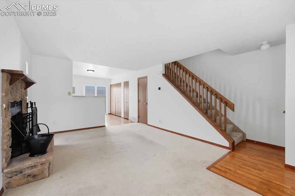 Unfurnished living room with a fireplace with raised hearth, light wood-style flooring, stairway, and light carpet