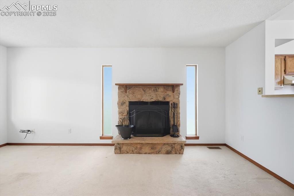 Unfurnished living room with a stone fireplace and carpet floors