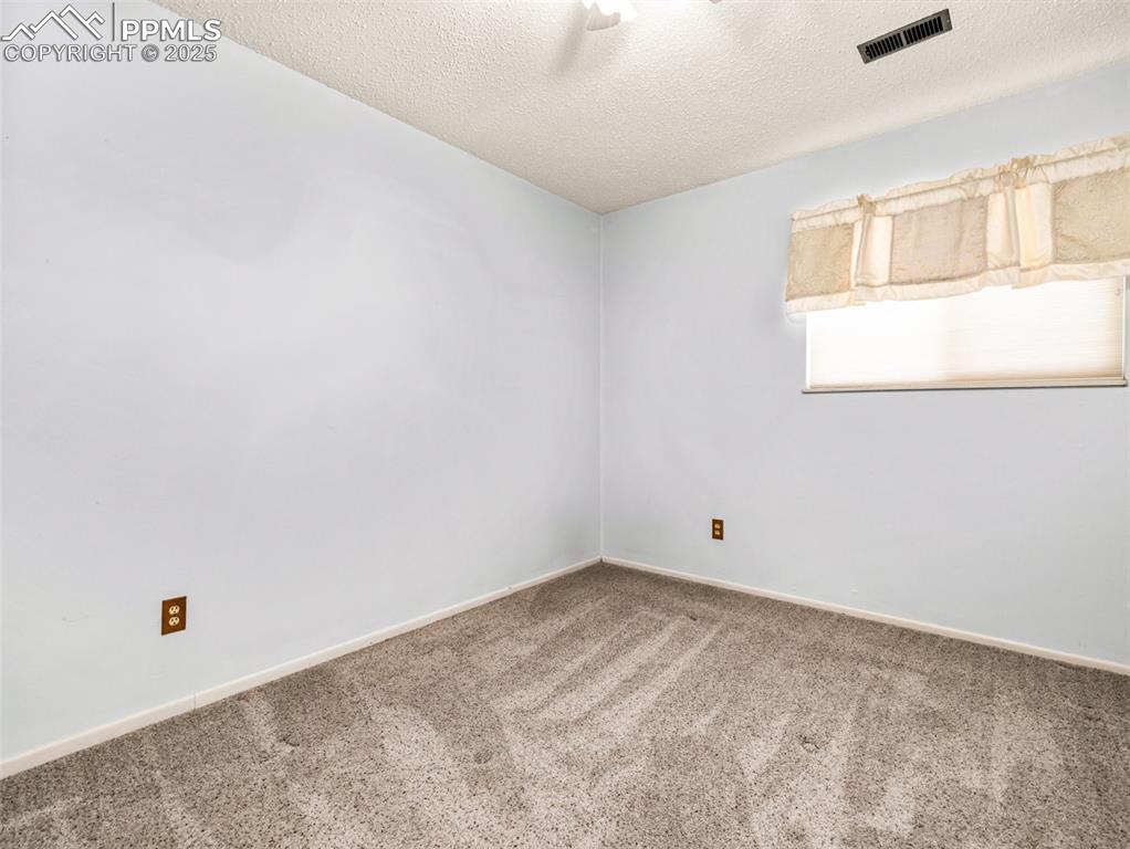 Carpeted empty room with a textured ceiling and baseboards