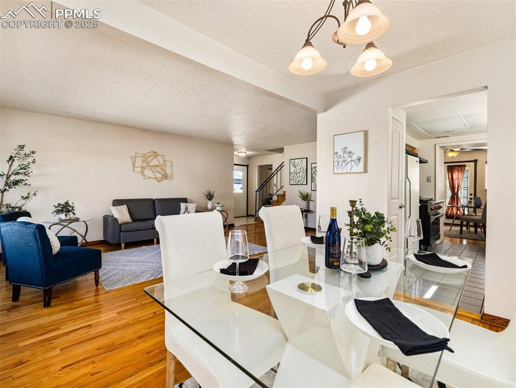 Dining area with a textured ceiling, stairway, light wood-style floors, and a chandelier