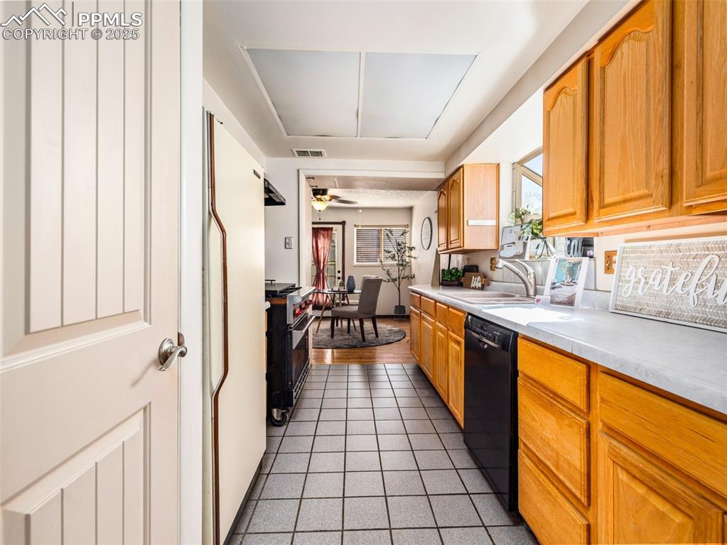 Kitchen with dark tile patterned flooring, black dishwasher, freestanding refrigerator, a ceiling fan, and light countertops