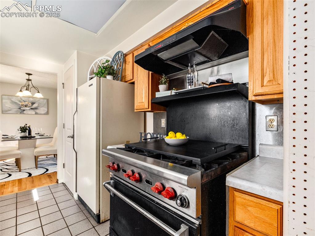 Kitchen featuring designer stove, light countertops, exhaust hood, light tile patterned floors, and freestanding refrigerator
