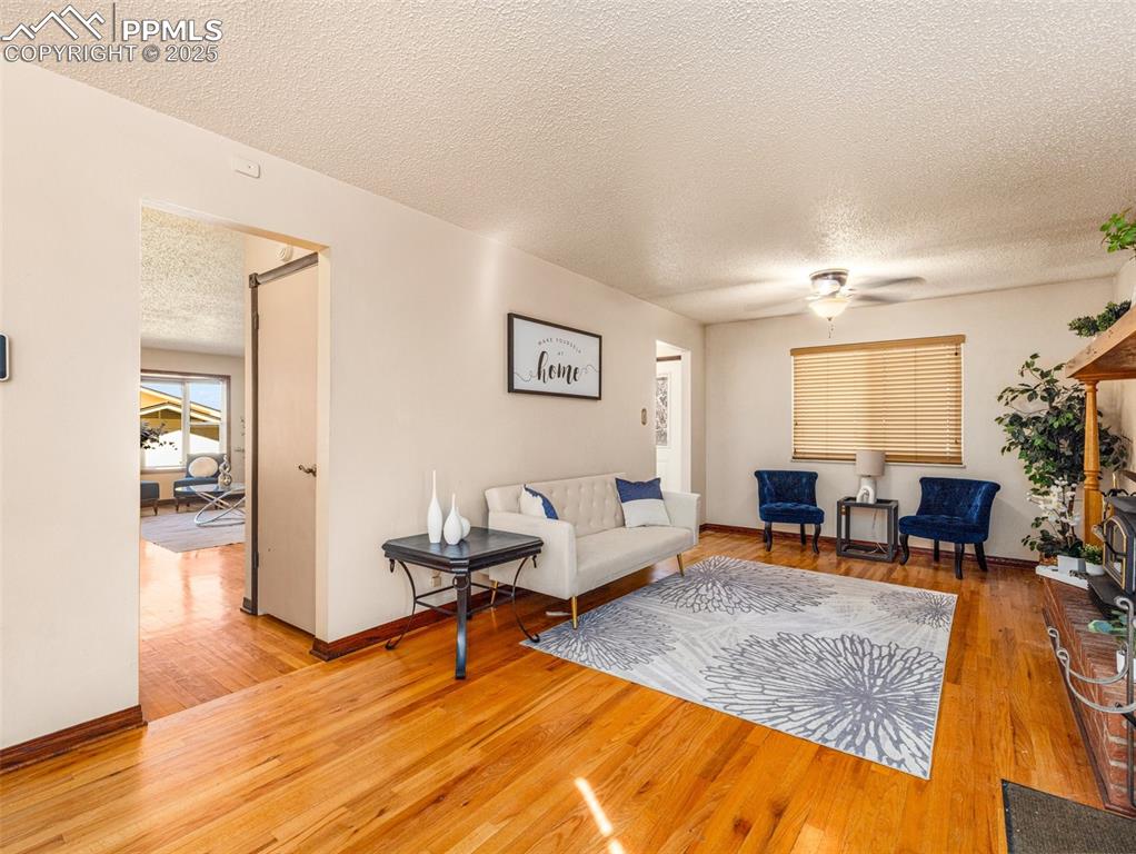 Living room with a textured ceiling, light wood-style flooring, and a ceiling fan