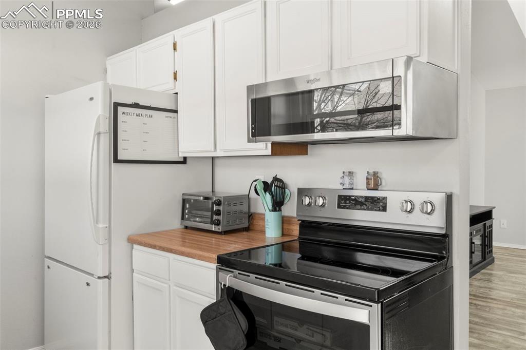 Kitchen featuring stainless steel appliances, white cabinets, light countertops, and light wood-type flooring
