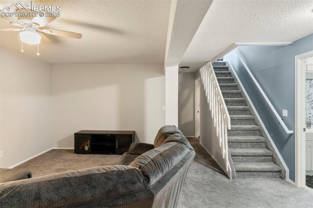 Living area with light colored carpet, a textured ceiling, and a ceiling fan