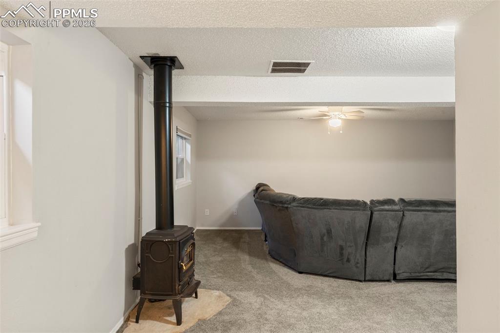 Carpeted living room with a textured ceiling, a ceiling fan, and a wood stove