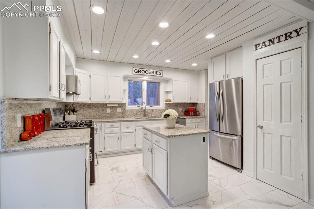 Kitchen featuring white cabinets, appliances with stainless steel finishes, light marble finish flooring, decorative backsplash, and wood ceiling