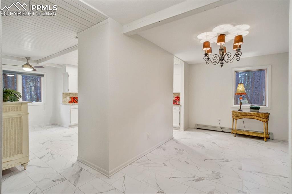 Dining area featuring beam ceiling, light marble finish flooring, a chandelier, and a baseboard heating unit