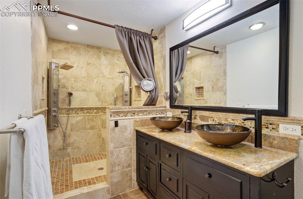 Full bathroom with a walk in shower, double vanity, recessed lighting, backsplash, and tile walls