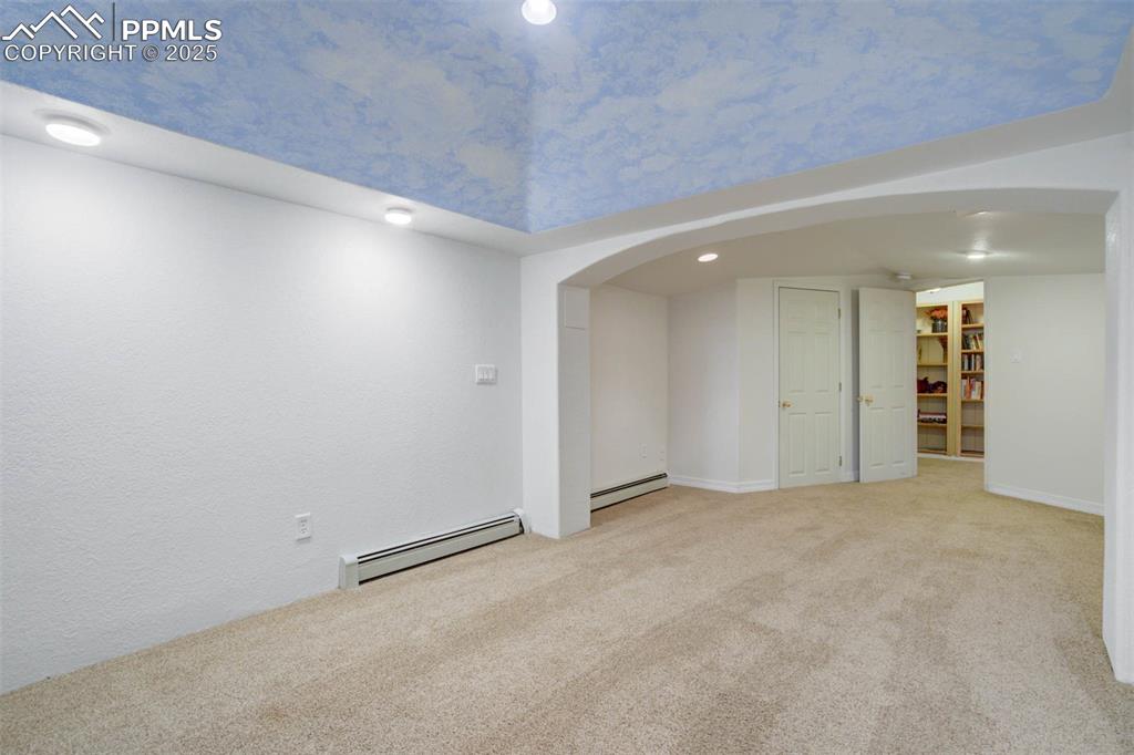 Empty room featuring arched walkways, carpet floors, a baseboard radiator, and recessed lighting