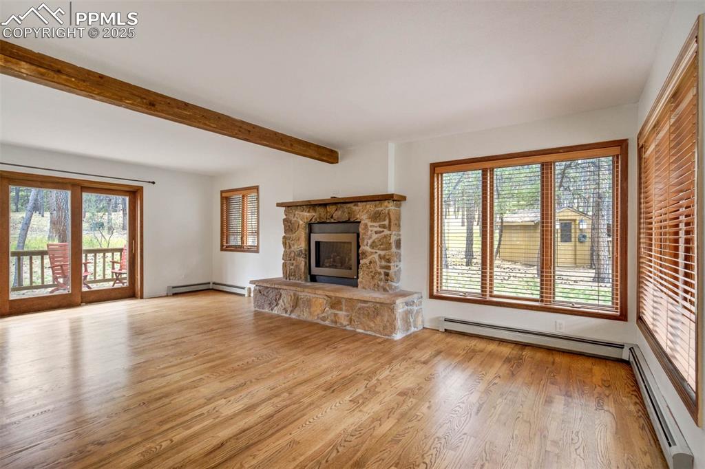 Unfurnished living room with light wood-style floors, a fireplace, baseboard heating, and beam ceiling