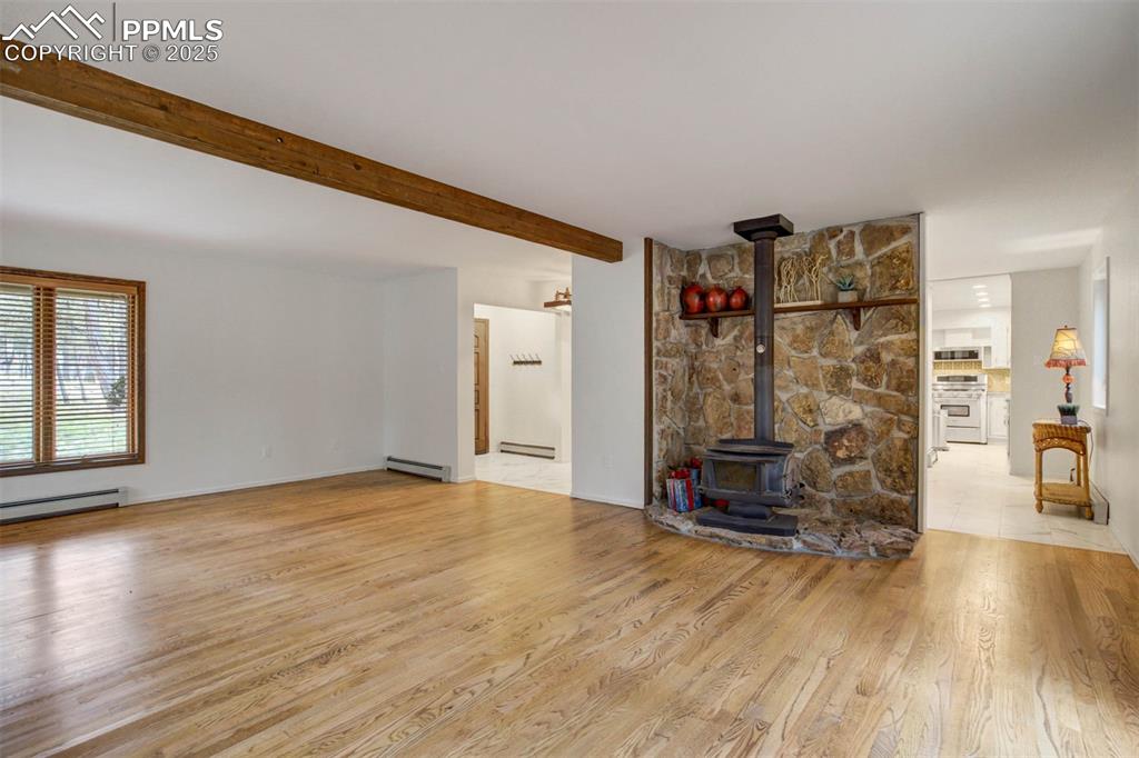 Unfurnished living room with a wood stove, light wood-style flooring, beam ceiling, and a baseboard radiator