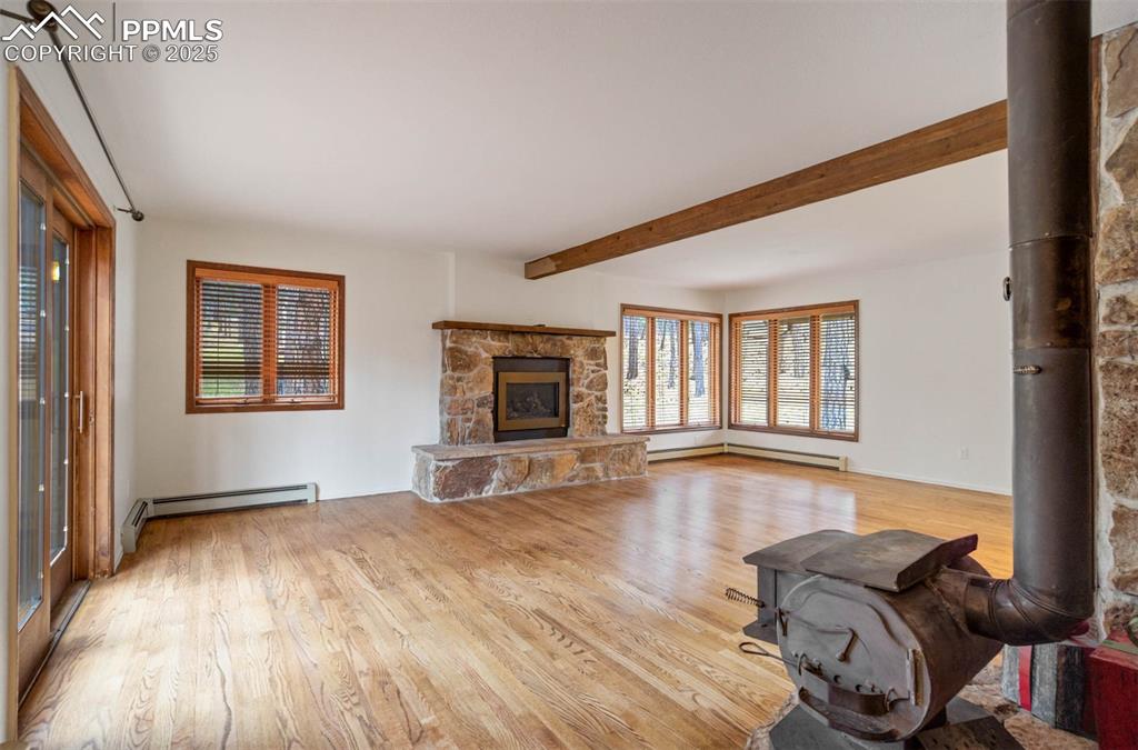 Living room featuring a wood stove, light wood-style floors, healthy amount of natural light, and beamed ceiling