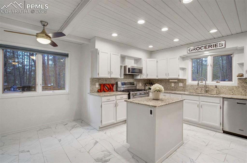 Kitchen featuring open shelves, decorative backsplash, white cabinetry, appliances with stainless steel finishes, and a kitchen island