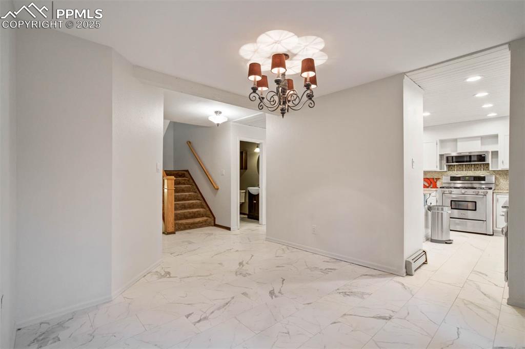 Unfurnished dining area featuring light marble finish flooring, a chandelier, stairs, recessed lighting, and a baseboard heating unit