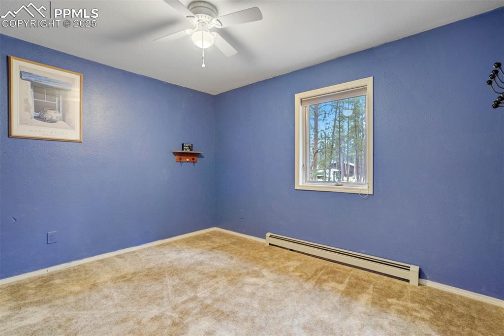 Carpeted empty room with a baseboard radiator, a ceiling fan, and a textured wall