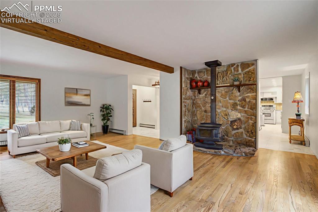 Living room with a wood stove, beamed ceiling, light wood-style floors, a baseboard heating unit, and a baseboard radiator, virtually staged
