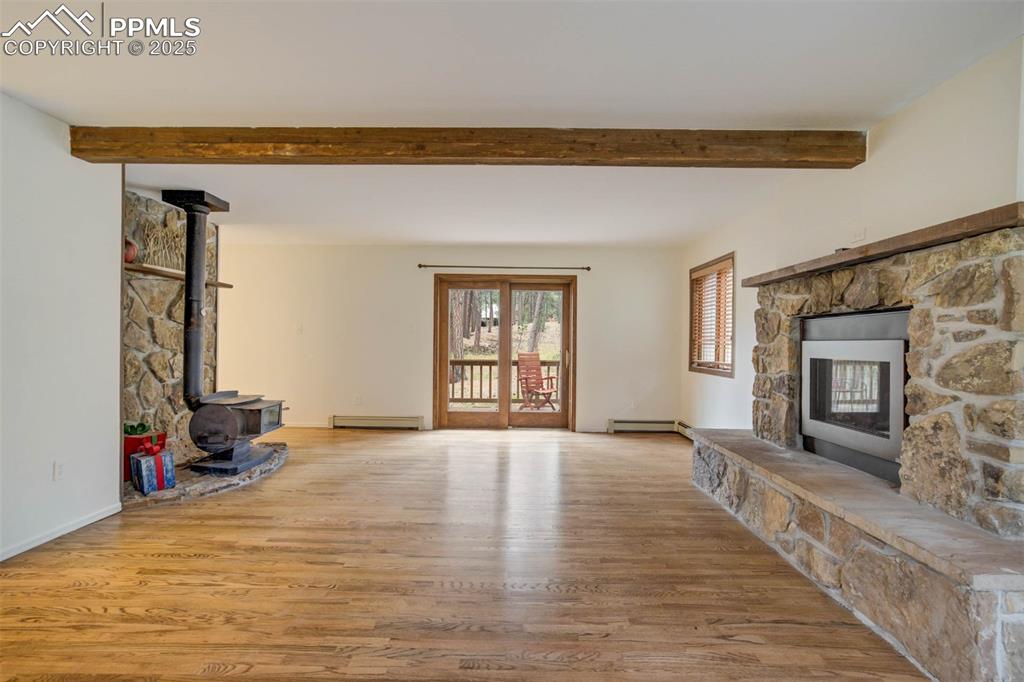 Unfurnished living room featuring a wood stove, light wood-style flooring, a fireplace, beam ceiling, and a baseboard radiator