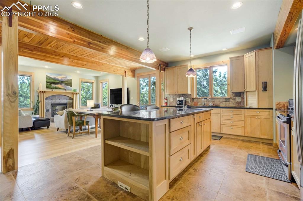 Kitchen with light birch cabinetry, beamed ceiling, open floor plan, granite slab counters and decorative backsplash