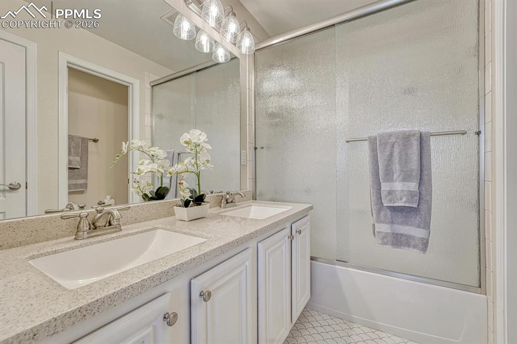 Full primary bathroom has double vanity, granite counter, and decorative tile floor