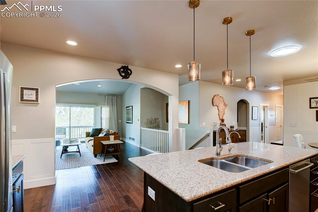 Kitchen with dark brown cabinetry, open floor plan, arched walkways, pendant lighting, and light stone counters