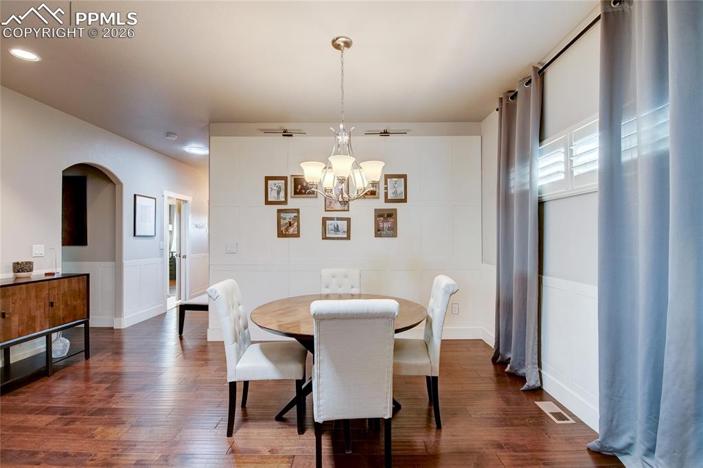 Dining space featuring dark wood-style floors, arched walkways, a chandelier, and wainscoting