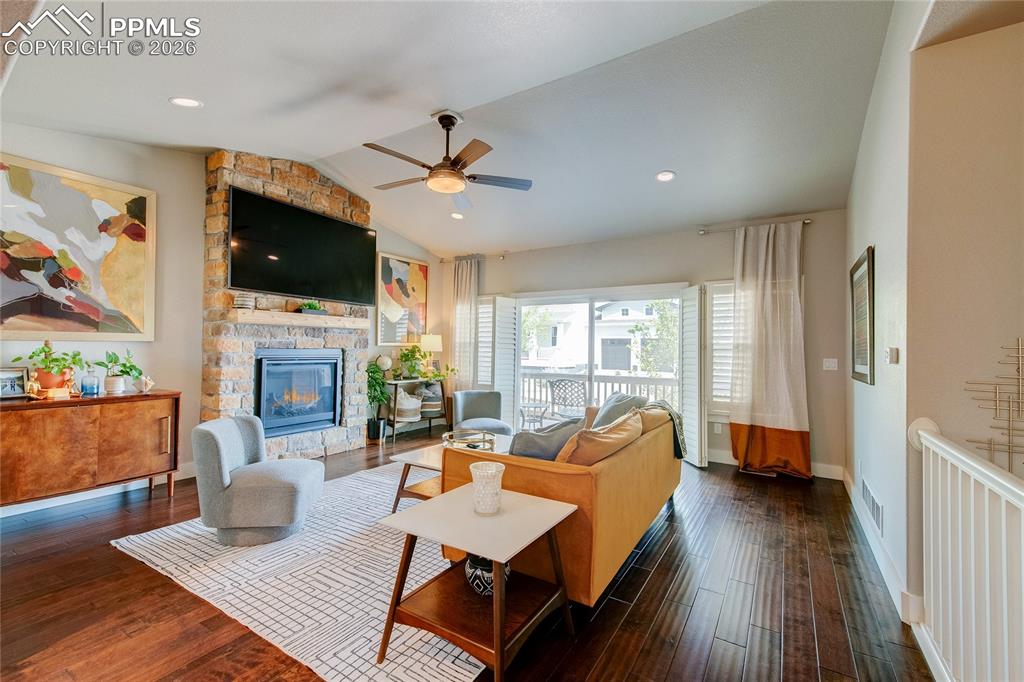 Living room with a fireplace, vaulted ceiling, dark wood-type flooring, ceiling fan, and recessed lighting