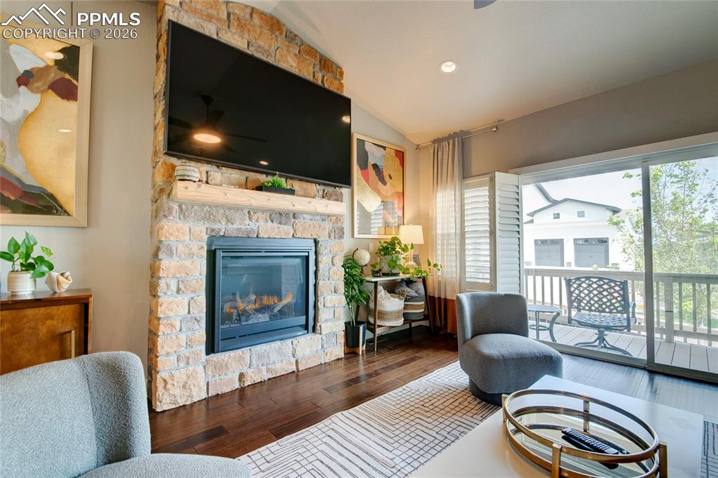 Living room with vaulted ceiling, wood-type flooring, a ceiling fan, a stone fireplace, and recessed lighting