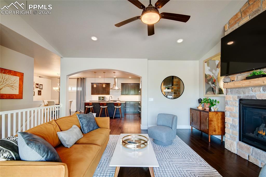 Living room featuring dark wood-type flooring, arched walkways, a fireplace, a ceiling fan, and recessed lighting