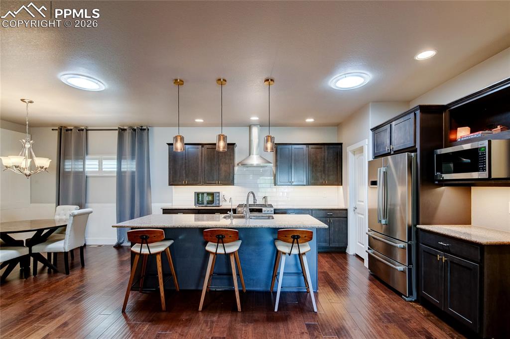 Kitchen with a kitchen bar, stainless steel appliances, pendant lighting, decorative backsplash, and light stone countertops