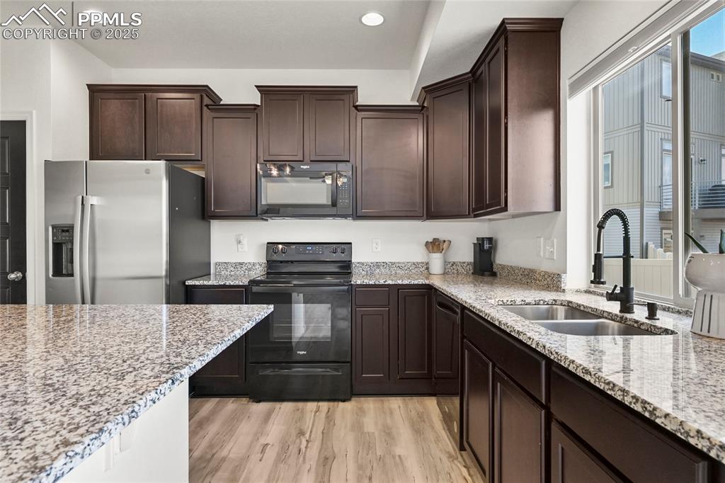 Kitchen featuring black appliances, dark brown cabinetry, light wood-type flooring, light stone countertops, and recessed lighting