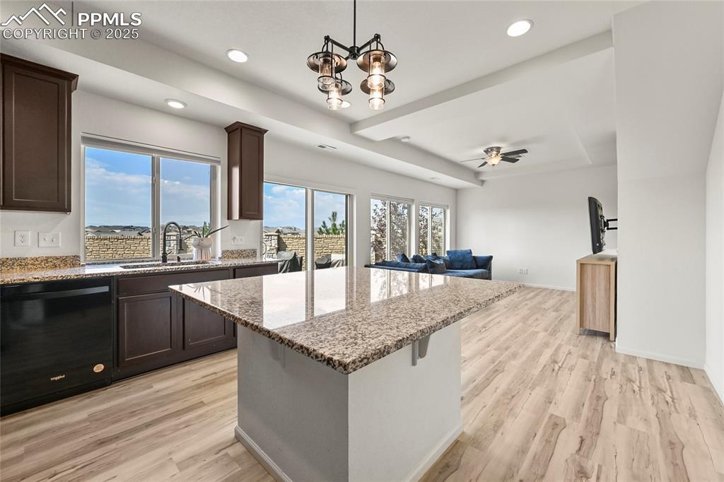 Kitchen with dishwasher, light stone counters, open floor plan, dark brown cabinets, and recessed lighting
