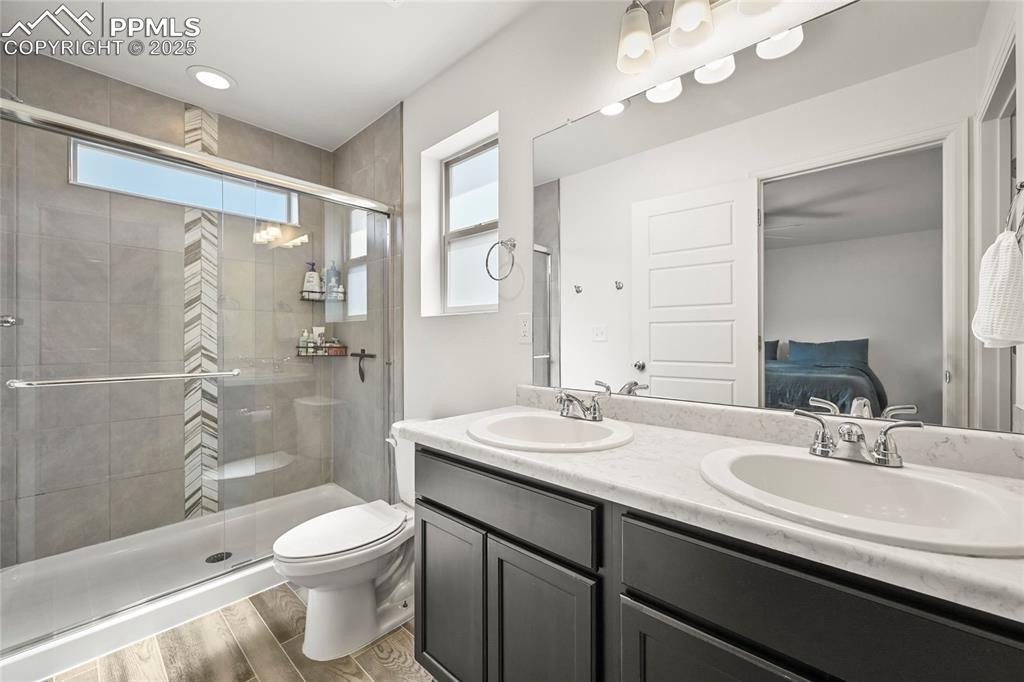Ensuite bathroom with a stall shower, light wood-style floors, healthy amount of natural light, double vanity, and recessed lighting