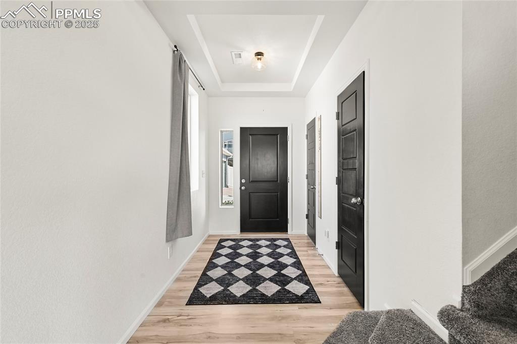 Doorway with a raised ceiling and wood finished floors
