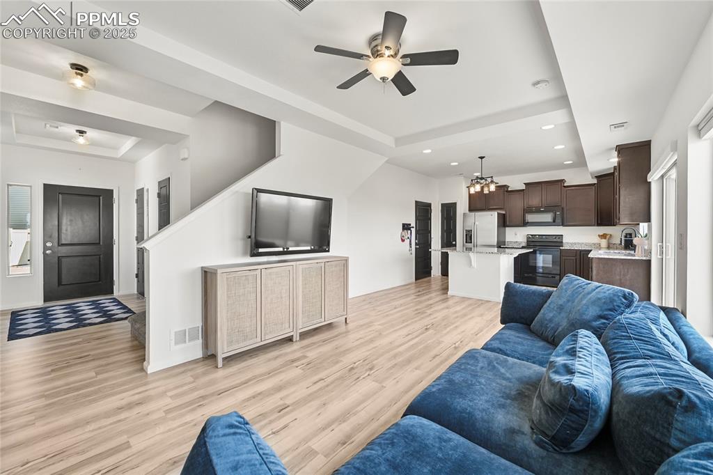 Living room featuring a raised ceiling, light wood-style flooring, recessed lighting, and ceiling fan