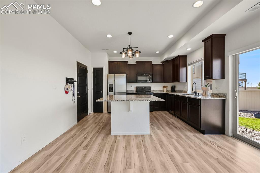 Kitchen with pendant lighting, dark brown cabinets, light wood finished floors, light stone counters, and recessed lighting