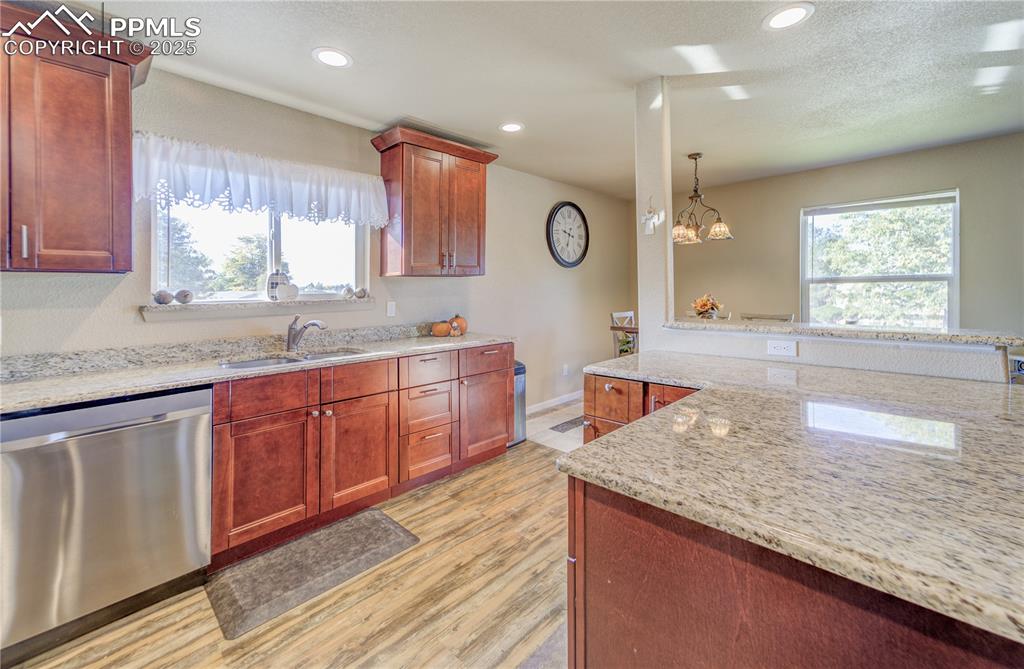 Kitchen featuring light wood-type flooring, light stone countertops, stainless steel dishwasher, & sink