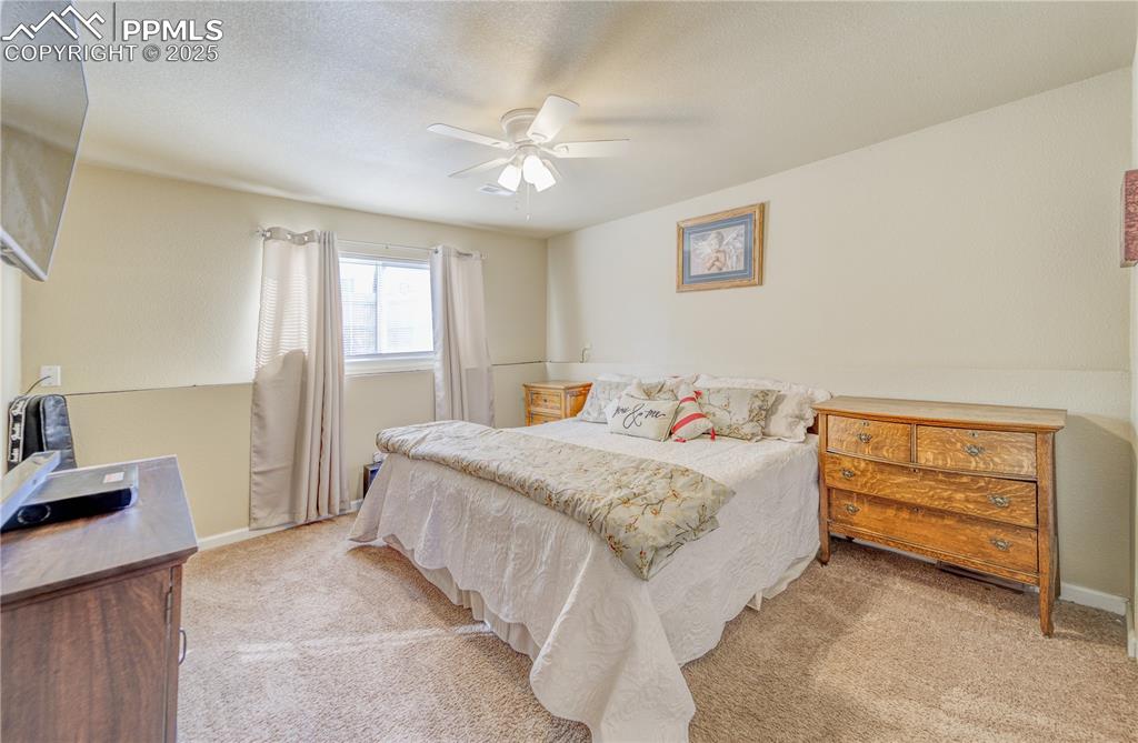 Bedroom with ceiling fan, light colored carpet, and a textured ceiling